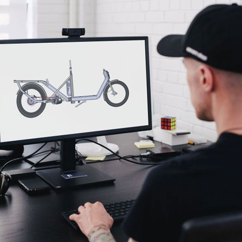 Vue en studio d'un homme travaillant sur la conception du vélo électrique cargo devant un écran